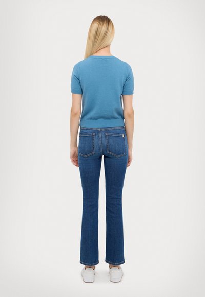 Blå kortermet strikket genser kombinert med lys blå jeans med vide ben. Jeansene har baklommer og lyse sømdetaljer. Hvite joggesko er synlige.