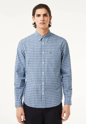 Camisa de botones en un patrón de cuadros azul y blanco, de manga larga, con cuello clássico y un pequeño logo verde en el pecho. Tejido de algodón.