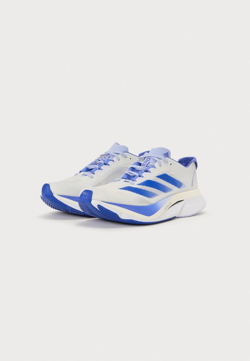 Scarpe sportive bianche con accenti blu, dotate di una tomaia in mesh traspirante, suola testurizzata e logo a tre strisce sul lato.