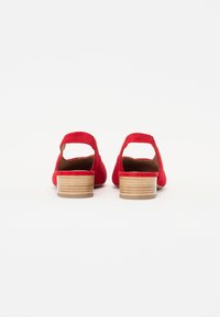 Tacchi in suede rosso con punta arrotondata, apertura sul retro e tacco in legno impilato. Presentano una cinghia alla caviglia per un ulteriore supporto.
