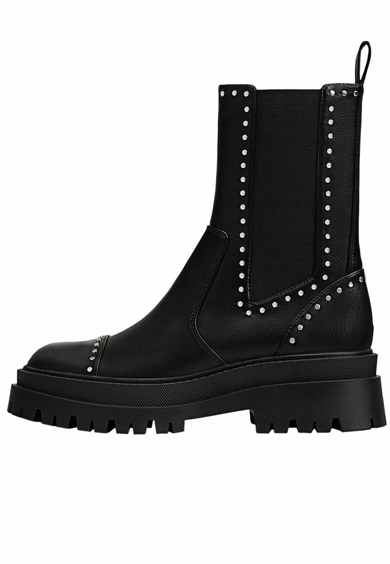 Bottes noires à la cheville avec une semelle épaisse, dotées d'une surface extérieure en cuir lisse, de panneaux latéraux élastiques et de clous argentés le long des coutures.