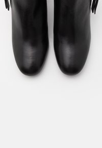 Paire de bottines en cuir noir avec bouts arrondis et fermetures éclair latérales, vues de dessus sur un fond blanc.
