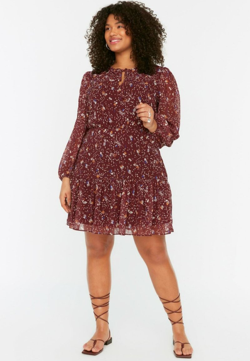 Robe florale bourgogne avec de longues manches bouffantes, un décolleté en trou de serrure et une jupe à volants superposés ; accompagnée de sandales à lanières marron.