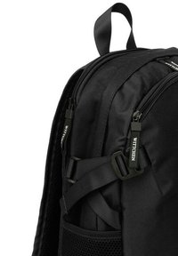 Zaino in nylon nero con superficie texturizzata, doppie cerniere, spallacci regolabili e tasca laterale in rete. Caratterizzato da tirazip con marchio e manico robusto.