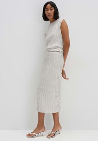 Light beige pleated outfit featuring a sleeveless top and mid-length skirt. The smooth texture and subtle lines create an elegant design. Silver sandals.