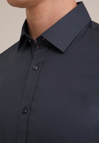 Camisa de botones azul marino con un cuello estructurado, textura suave y botones visibles, que presenta un detallado bordado a lo largo de la tapeta.