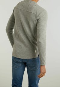Graues Langarmshirt mit nahtlosem Schulterdesign, abgerundetem Saum und strukturiertem Stoff. Kombiniert mit blauen Jeans.