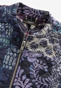 Gequilted jas met gemengde blauwe en paarse bloemen- en abstracte patronen, zilveren rits gedeeltelijk dicht, en zwart NEXT-label op de kraag.