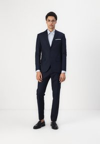 Navy suit with a tailored design, featuring a single-breasted jacket, notch lapels, and a light blue shirt. Black loafers complete the look.