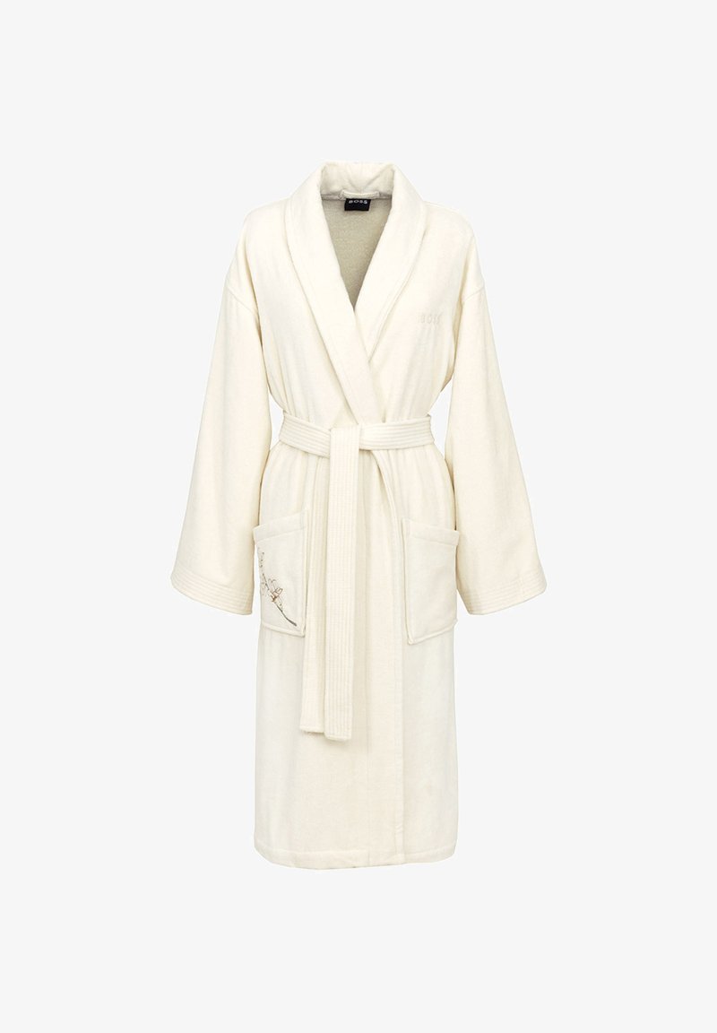 Peignoir en peluche couleur crème avec col châle, ceinture à la taille et deux poches avant, l'une des poches présentant une broderie florale subtile.