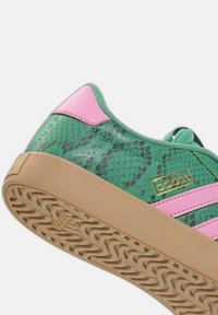 Sneaker verde con motivo a pelle di serpente testurizzata, dettagli rosa, logo dorato e suola in gomma beige con battistrada ondulato.