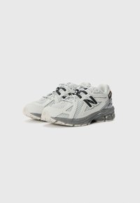 Pantofi sport gri cu părți din plasă, șireturi negre și talpă texturată. Au un logo distinctiv și un călcâi cu pernuță.