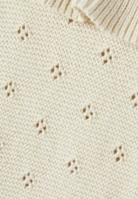 Tessuto lavorato a maglia leggero color beige chiaro con un motivo testurizzato e piccole accentuazioni marroni. Il bordo presenta dettagli a costine per aggiungere texture.