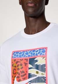 Camiseta blanca de algodón con un diseño gráfico colorido que incluye estampados de animales y patrones abstractos sobre un fondo cuadrado, delineado en rosa.