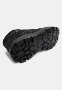 Zapato de ante negro con una suela de goma texturada que presenta profundos surcos para tracción y costuras contrastantes en la parte superior.