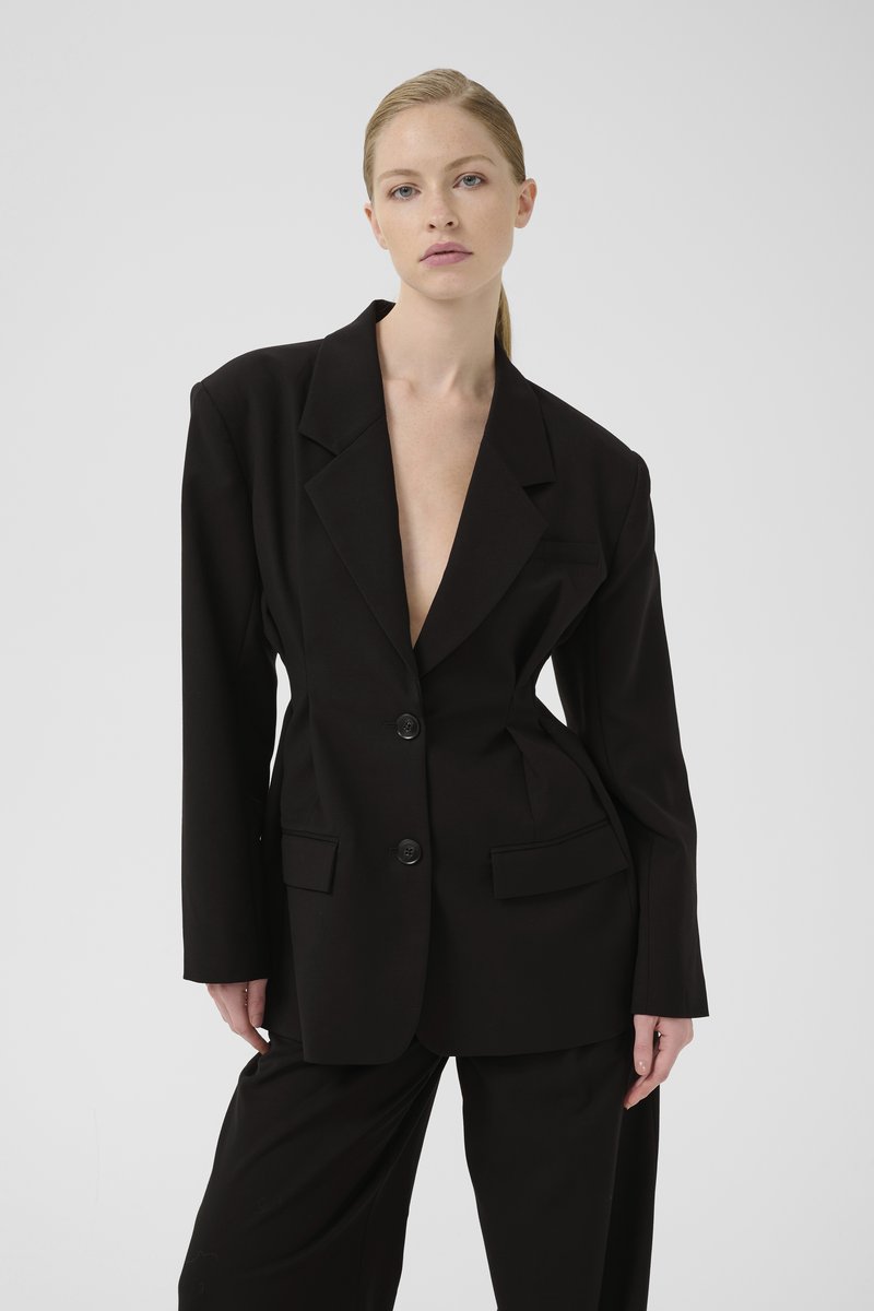 Svart oversized blazer med spisse slag, to frontlommer og dobbel knappelukking. Glatt stoff med en strukturert silhuett.