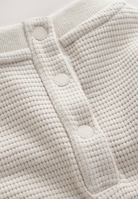 Beige strukturerad stickad skjorta med en vertikal knappslå med fyra knappar, ribbat krage och mjön, vävd mönster.