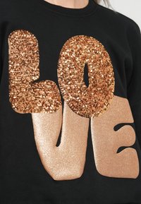 Μαύρη μπλούζα με μεγάλο γραφικό "LOVE". Τα γράμματα έχουν υφή από χρυσά παγιέτα και με ένα λαμπερό ροζ χρυσό φινίρισμα.