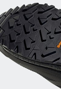 Gros plan de la semelle noire d'une chaussure avec un motif profond de bande de roulement géométrique et un petit logo orange "Continental" sur une surface texturée.