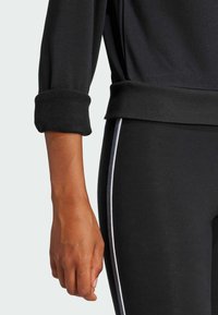 Svart idrottströja med rullade ärmar och ribbat mudd, tillsammans med svarta leggings med en kontrasterande vit sidremsa.