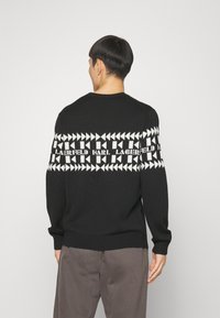 Czarny sweter z dzianiny z białym geometrycznym wzorem i nazwą marki na piersi. Ściągacze przy mankietach i u dołu, okrągły dekolt.