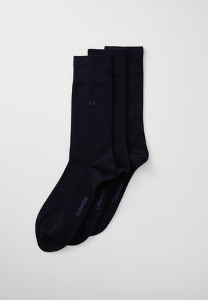 Trois paires de chaussettes en coton bleu marine, avec une texture lisse, présentant de petits logos blancs imprimés sur le côté et des poignets côtelés.