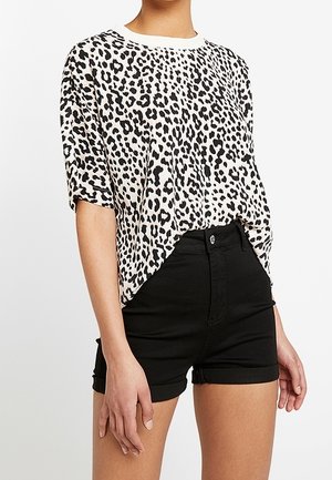 Femme portant un haut ample à manches courtes imprimé léopard, rentré dans un short en denim noir taille haute avec ourlets retroussés.