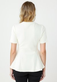 Top peplum bianco realizzato in tessuto morbido, con maniche corte e scollatura rotonda. Presenta un orlo svasato e cuciture a punta sul retro.