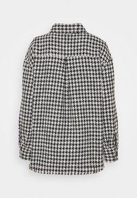 Mustat ja valkoiset houndstooth-kuvioiset paidat, joissa on kaulus, nappikahvat ja löysä istuvuus. Tekstuuri näyttää kudotulta ja karhealta.