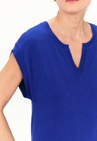 Suéter azul de punto con mangas cortas, que presenta un escote en V y una textura suave. El diseño enfatiza un estilo simple y casual.