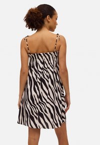 Vestido de rayas en blanco y negro con tirantes ajustables, cuerpo fruncido y falda de corte acampanado que cae por encima de la rodilla. Textura de tejido suave.