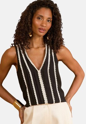 Top nero senza maniche con scollatura a V, caratterizzato da un bordo in pizzo bianco verticale e un design in tessuto testurizzato, abbinato a pantaloni color crema.