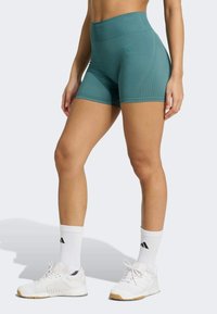 Shorts de sport taille haute teal avec une texture lisse et un design à rayures sur les côtés, associés à des baskets blanches et des chaussettes de cheville.