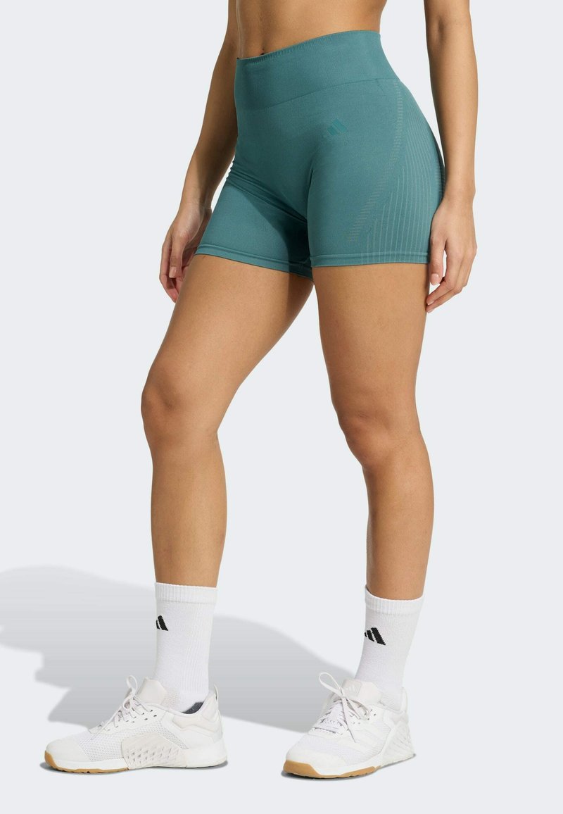 Shorts de sport taille haute teal avec une texture lisse et un design à rayures sur les côtés, associés à des baskets blanches et des chaussettes de cheville.