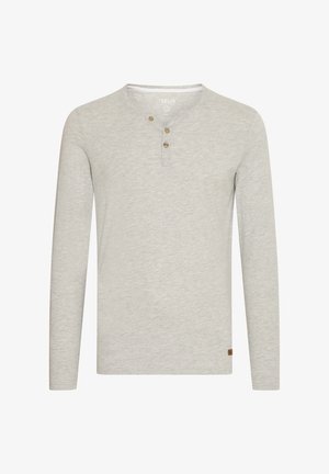 Jasnoszara koszula z długimi rękawami, wykonana z miękkiego materiału, z okrągłym dekoltem, trzema drewnianymi guzikami i małą brązową naszywką z logo u dołu.