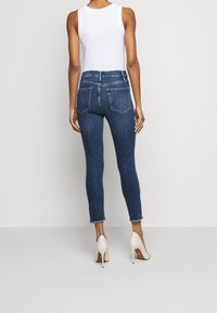 Jeans oscuros de talle alto con corte ajustado, que presentan una longitud de tobillo recortada, un ligero desgastado y bolsillos traseros.