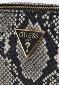 Portfel we wzór wężowej skóry w czerni i bieli z złotym logo w kształcie trójkąta z napisem "GUESS U.S.A." oraz symbolem znaku zapytania.
