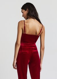 Haut en velours rouge à fines bretelles, assorti à un pantalon taille haute en velours rouge avec poches arrière. Texture lisse avec un design élégant.
