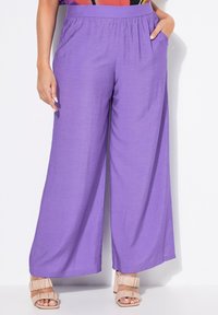 Paarse wijde broek met een elastische tailleband, voorzien van zijzakken en een lichtgewicht, gestructureerde stof. Gepaard met beige sandalen.