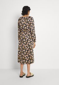 Dlouhá květinová šaty s dlouhým rukávem v černé barvě s oranžovými a žlutými květy, s nařaseným pasem a délku po kotníky. Noseny s jednoduchou obuví na klipsy.