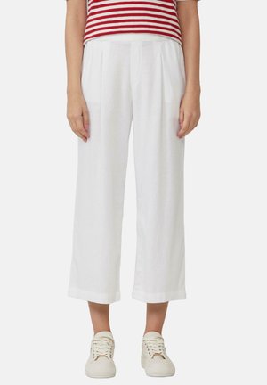 Culottes en lin blanc avec des plis, offrant une coupe décontractée et une longueur raccourcie, assortis à des baskets de couleur claire.
