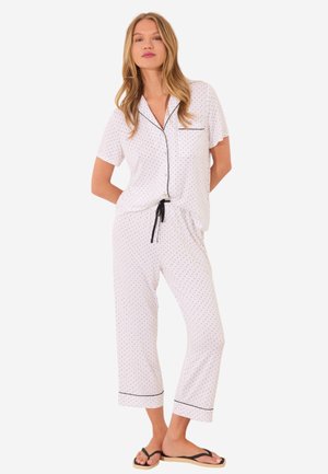 Weißes kurzärmliges Pyjama-Set mit schwarzen Polka-Dots und Besatz. Enthält ein kurzärmeliges Oberteil mit Knopfverschluss, eine Tasche und locker sitzende, cropped Hosen.