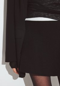 Musthave mustriga mustka, millel on tekstuuriga kudumismaterjal, koos musta pika varrukaga ülikonnaga, millel on valge soonik, ja kohandatud musta manteliga.