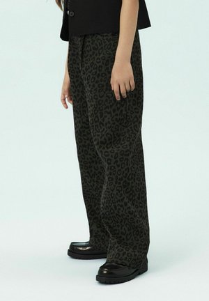 Pantalons à pattes larges imprimés léopard en vert foncé et noir, en tissu doux, associés à des chaussures noires à petit talon brillantes.