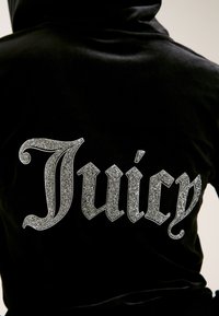 Fekete kapucnis sweatshirt, hátul nagy, csillogó ezüst csillámtollal írt "Juicy" felirattal, díszes betűtípussal. Puha tapintás, laza dizájn.