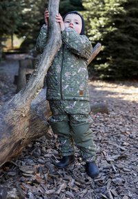 Rohelistest lillemustritest kamuflaažist isoleeritud jakk ja püksid, kantud mustade kummisaabastega, looduslikus väliskeskkonnas.