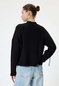 Zwarte rib gebreide sweater met een hoge hals, verlaagde schouders en een gestructureerde stof. Gecombineerd met lichtblauwe distressed jeans.