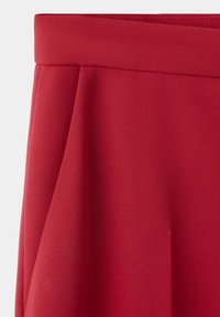 Jupe rouge avec une large ceinture et des plis souples, en tissu lisse de poids moyen.