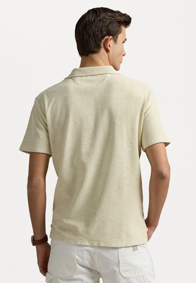 Polo-shirt van lichtbeige stof met een gestructureerd oppervlak, korte mouwen en een zachte kraag. De pasvorm is ontspannen, zonder zichtbare patronen.