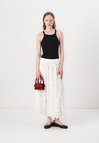 Zwart mouwloos topje, lange rok met witte bloemenborduring, rode handtas en zwarte ballerina's. Eenvoudig ontwerp met gladde texturen en contrasterende kleuren.